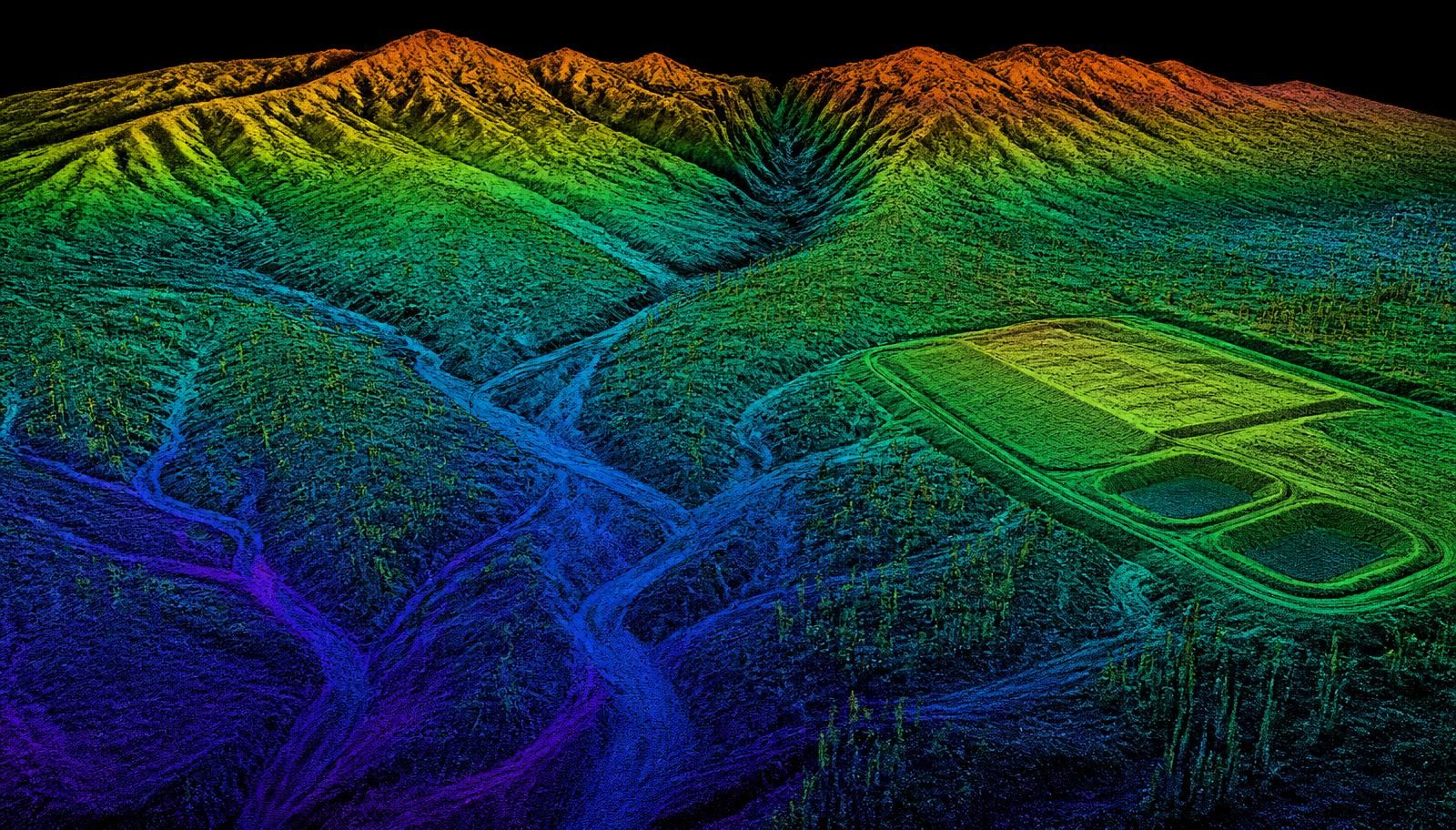 Arizona Sonoran Desert washes, bajada slopes, a graded development pad with detention basins, and an eroded mountain range rendered as a colorized aerial LiDAR point cloud